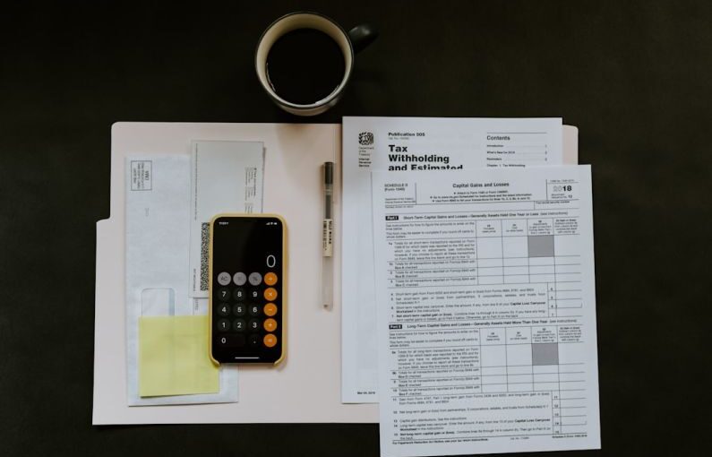 Tax - black Android smartphone near ballpoint pen, tax withholding certificate on top of white folder