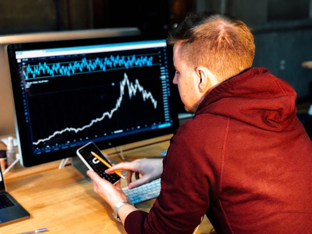 man-holding-black-smartphone-with-flat-screen-monitor-in-front